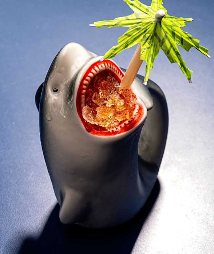Fruity drink served in a shark-shaped cup, garnished with a green umbrella.