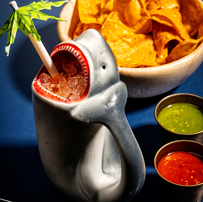 Shark-shaped cocktail mug with candy and straw, served with nachos and dipping sauces.