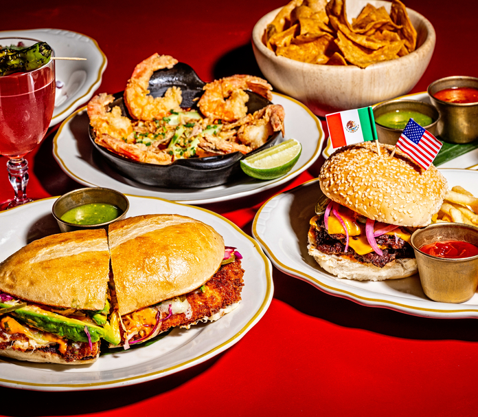 Tortilla chips, shrimp, chimichurri, and burgers with American and Mexican flags on a festive red tablecloth.